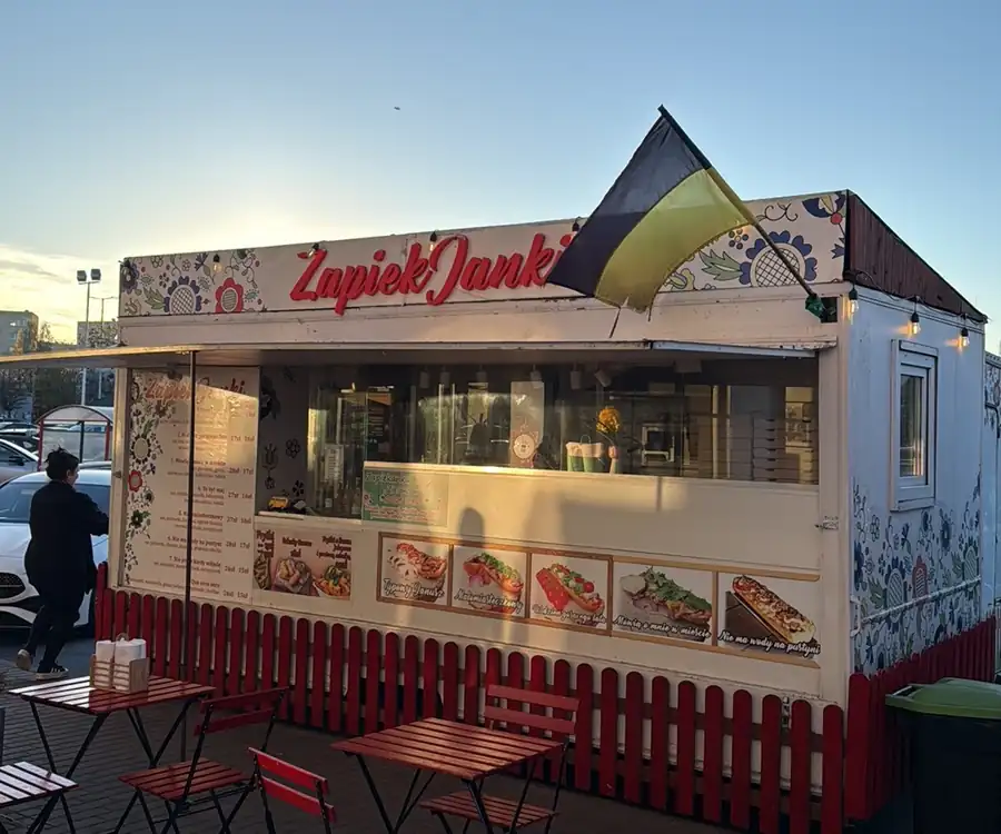 Kiosk ZapiekJanki z menu na ścianie i czerwonym płotkiem